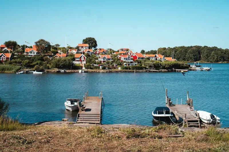 Rote Holzhäuser auf einer Schäreninsel bei Karlskrona, ein Steg mit Booten im blauen Wasser