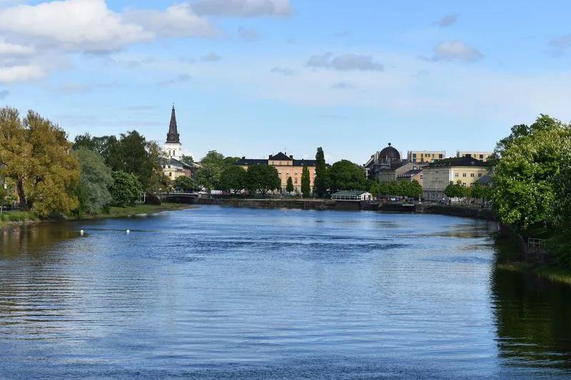Breiter Fluss im Sommer, am anderen Ufer ein Kirchturm, Bäume und helle Stadthäuser