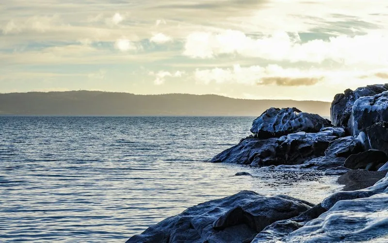 Felsiges Ufer am Vättern im goldenen Abendlicht, ruhiges Wasser, im Hintergrund das andere Ufer
