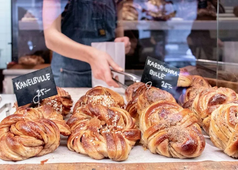 Zimtschnecken in einer Bäckerei, eine Hand mit Zange im Hintergrund