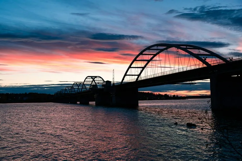 Eine Bogenbrücke über das Wasser bei Luleå im Abendrot, der Himmel leuchtet orange und blau