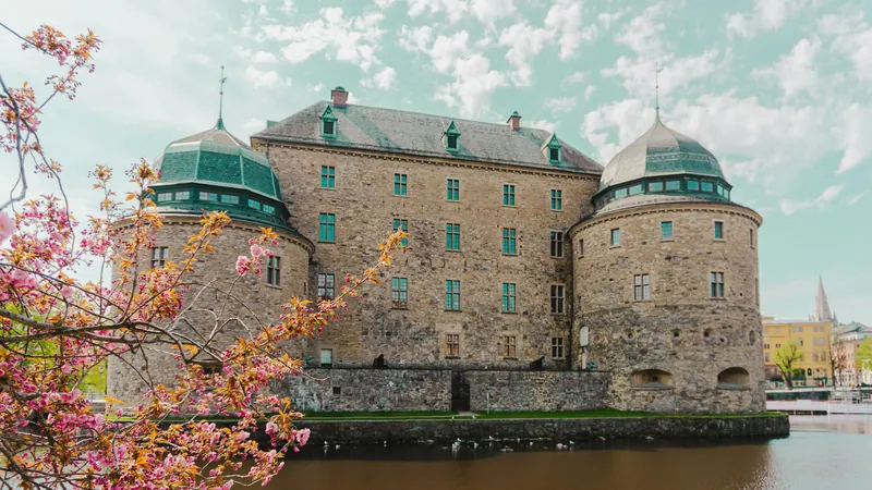 Das Schloss von Örebro hinter blühenden Zweigen am Fluss