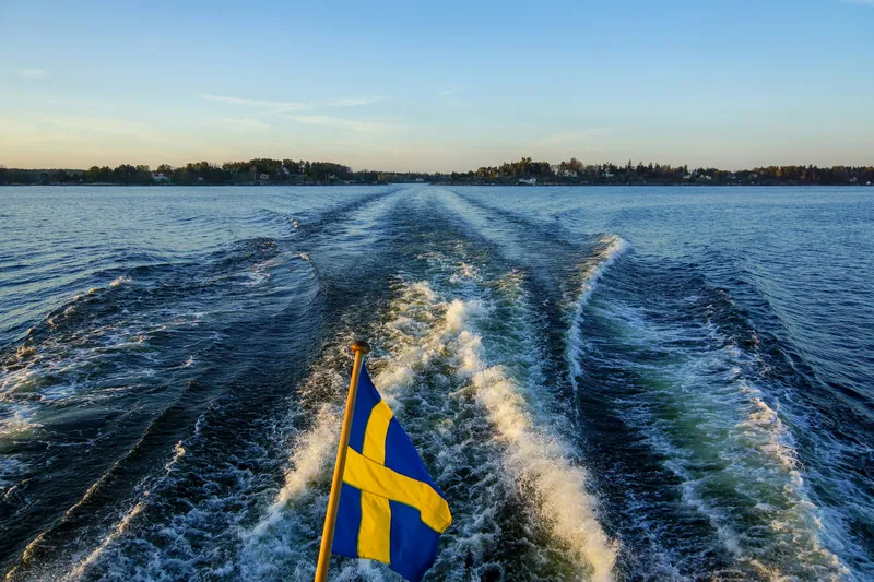 Stockholmer Schären, ein Boot mit schwedischer Flagge im Kielwasser