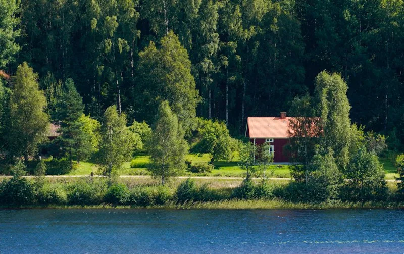 Rote Hütte zwischen Bäumen am Ufer eines Sees in Värmland