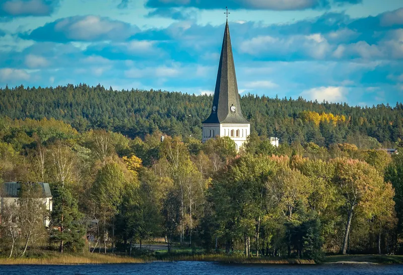 Die Kirche von Norberg ragt aus herbstlichem Wald am See