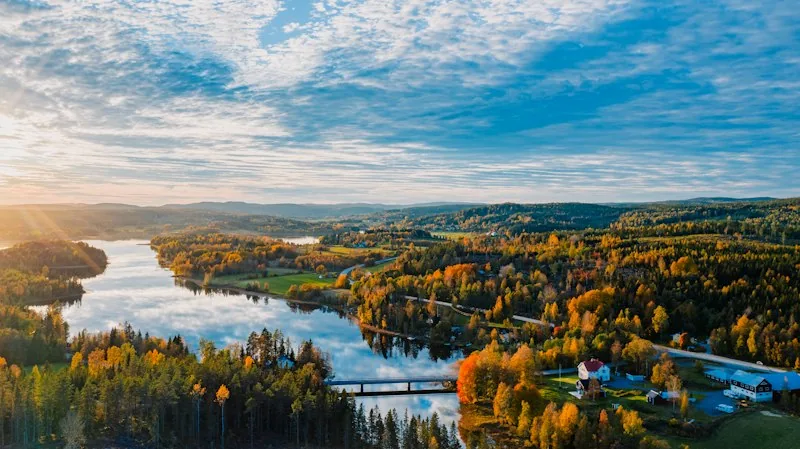 Luftbild: ein Fluss und Wälder in Herbstfarben im Abendlicht, ein Haus am Ufer